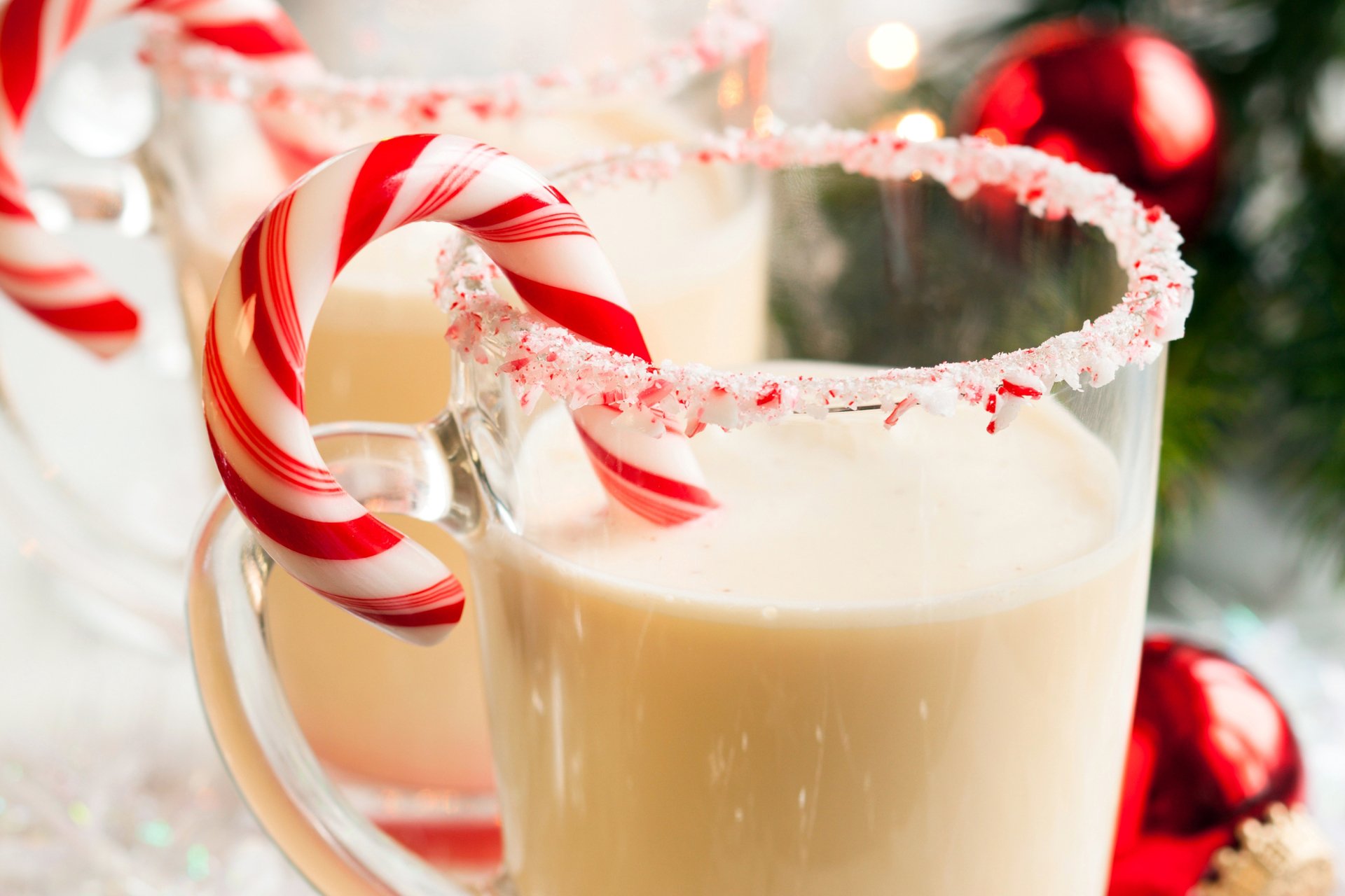 A festive HD wallpaper featuring glasses of milk adorned with crushed candy cane rims and striped candy canes, set against a holiday-themed backdrop with Christmas decorations.