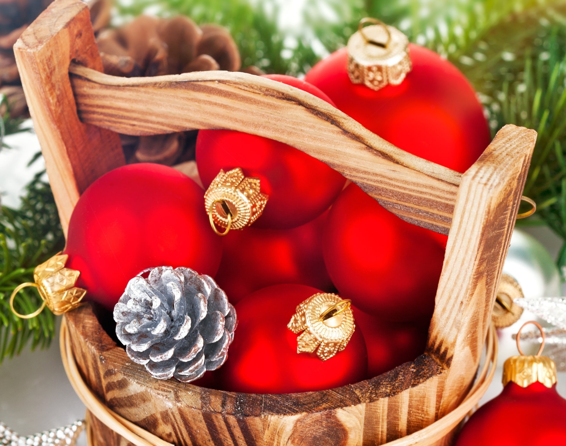 2K Quad HD PC desktop background: basket of red Christmas ornaments and a silver pine cone nestled in evergreen holiday foliage.