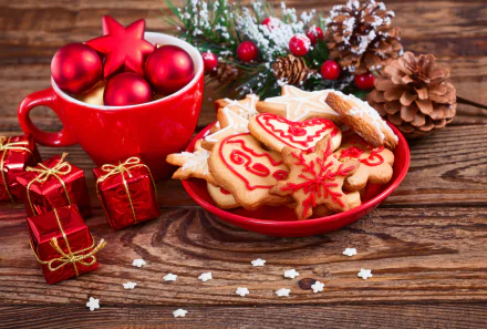 A festive 4K Ultra HD wallpaper featuring Christmas cookies, red ornaments in a mug, pine cones, and small wrapped gifts on a wooden holiday background.