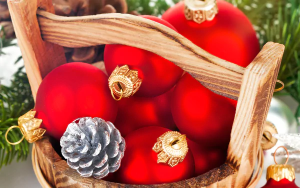 2K Quad HD PC desktop background: basket of red Christmas ornaments and a silver pine cone nestled in evergreen holiday foliage.