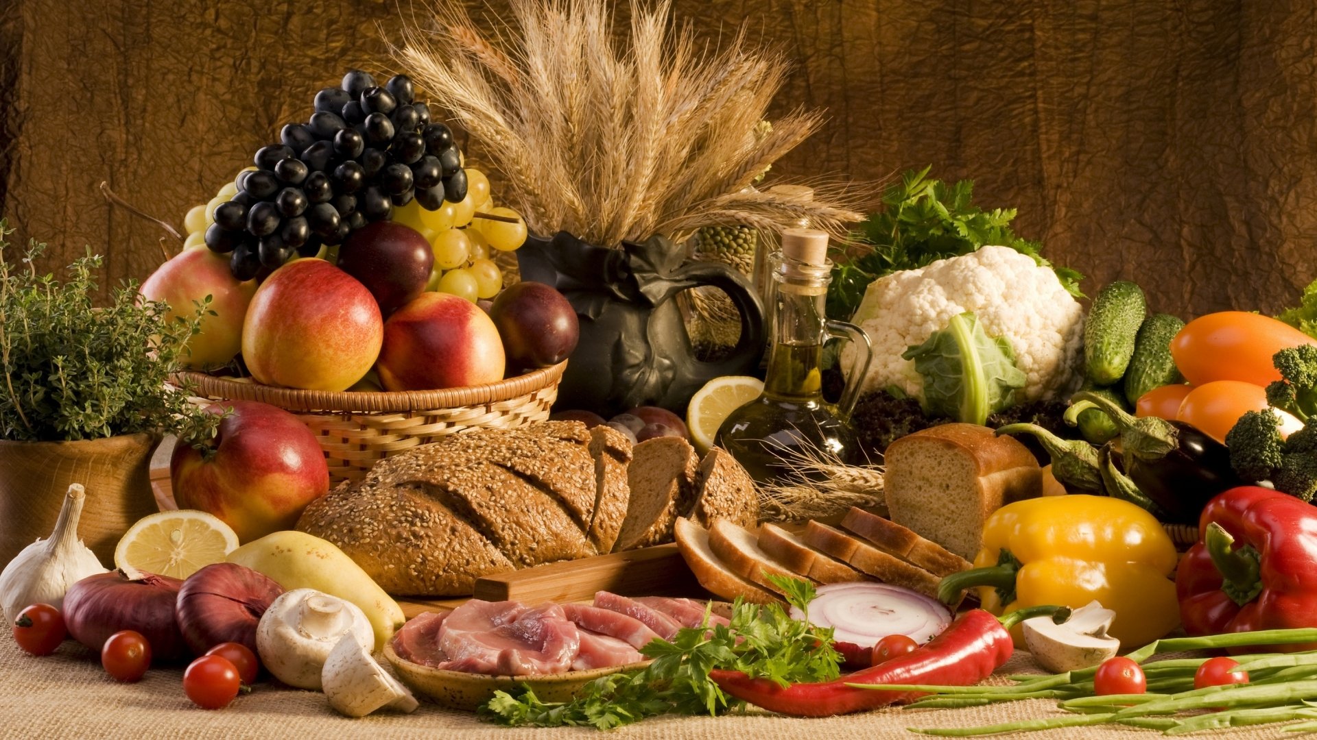 A vibrant still life of assorted fruits, vegetables, bread, meat, and garlic arranged with wheat stalks and olive oil on a rustic table, displayed as an HD PC desktop wallpaper.