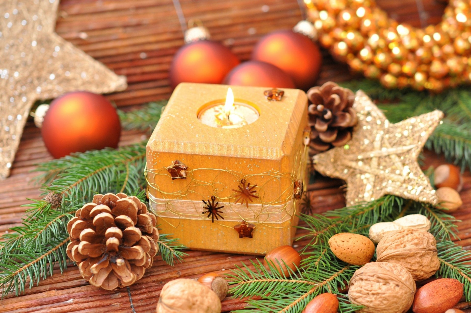 A holiday-themed HD desktop wallpaper featuring a lit candle surrounded by Christmas ornaments, pinecones, nuts, and festive greenery.