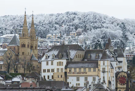 Snow-dusted Neuchâtel, Switzerland — historic church spires and man-made stone buildings set against wooded winter hills. 4K Ultra HD PC desktop wallpaper/background.