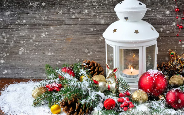 A cozy holiday scene featuring a white lantern surrounded by Christmas ornaments, pinecones, and snowy greenery, creating a festive atmosphere for desktop wallpaper.
