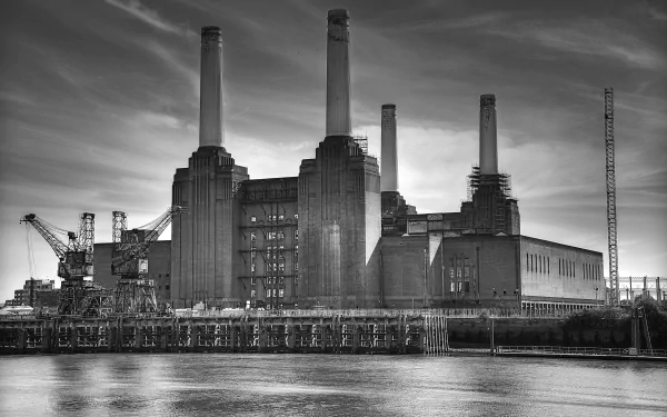 Black and white 4K Ultra HD image of a large industrial factory with tall chimneys by the water, showcasing man-made architecture and detailed structural elements.