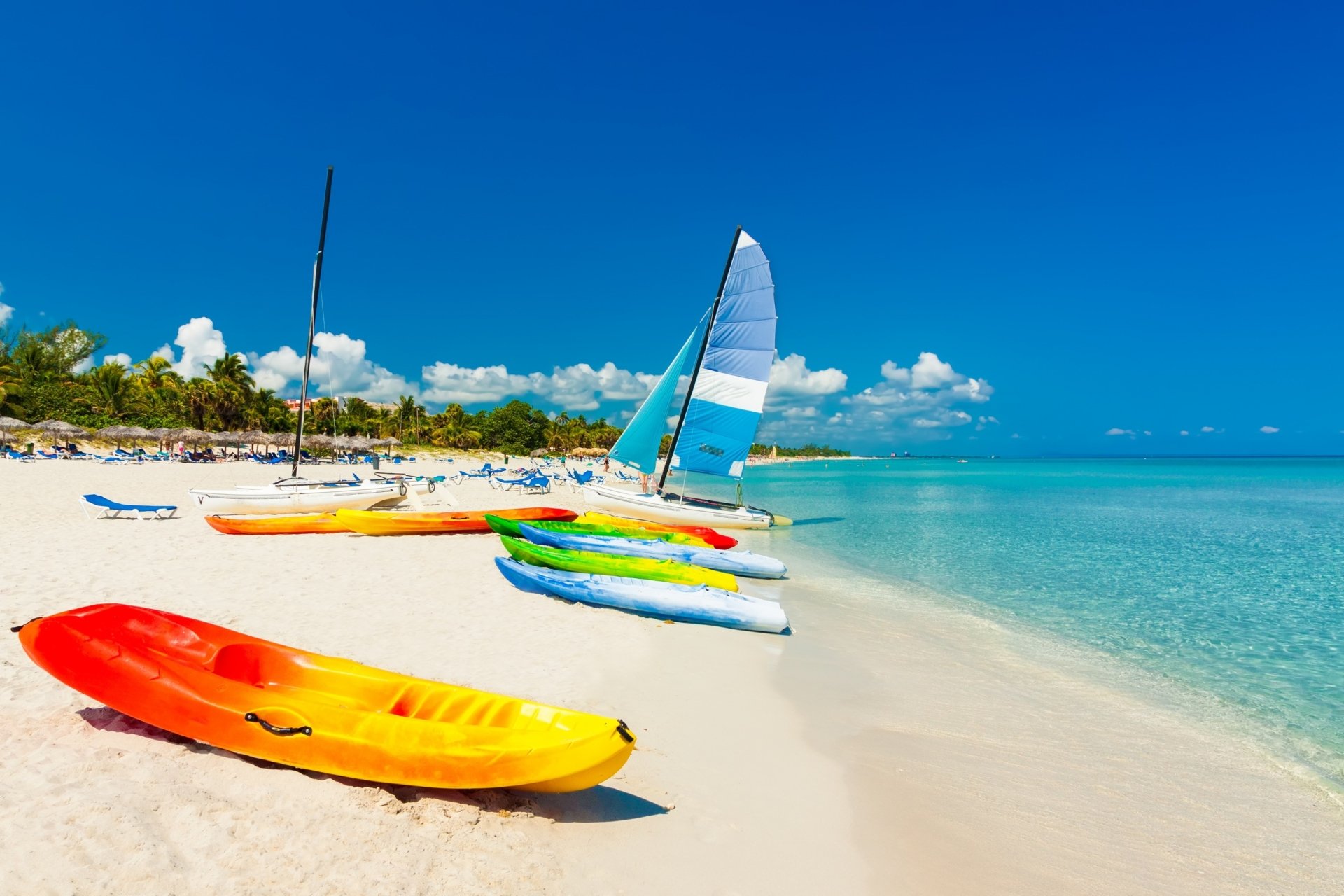 A vibrant tropical beach scene featuring colorful kayaks and sailboats along the ocean, under a clear blue sky, showcasing the essence of summer and adventure. Perfect HD wallpaper for your desktop.