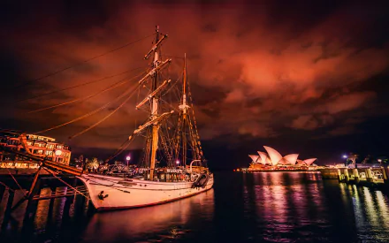 A majestic sailboat docked beside the Sydney Opera House, illuminated by a vibrant sky, captured in stunning 4K Ultra HD, creating a striking urban maritime scene.