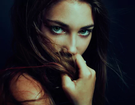 Close-up of a brunette woman with green eyes partially covering her face with her hair, captured in high-definition for a PC desktop wallpaper.