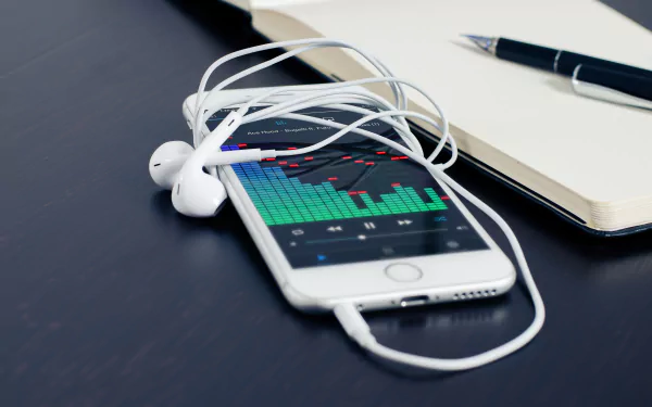 4K Ultra HD wallpaper featuring an Apple iPhone with white headphones resting on it, beside a notebook and pen, showcasing technology and audio elements.