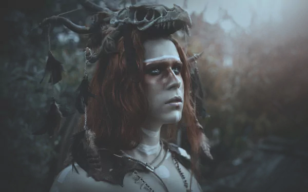 Dark artistic cosplay shaman: redhead woman model in a horned headdress and tribal paint, moody bokeh forest backdrop — HD PC desktop wallpaper/background.