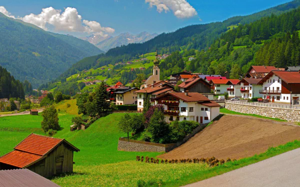 Bavarian mountain village panorama with clustered houses, church steeple and green pastures — man-made settlement framed by alpine slopes. 2K Quad HD PC desktop wallpaper background.