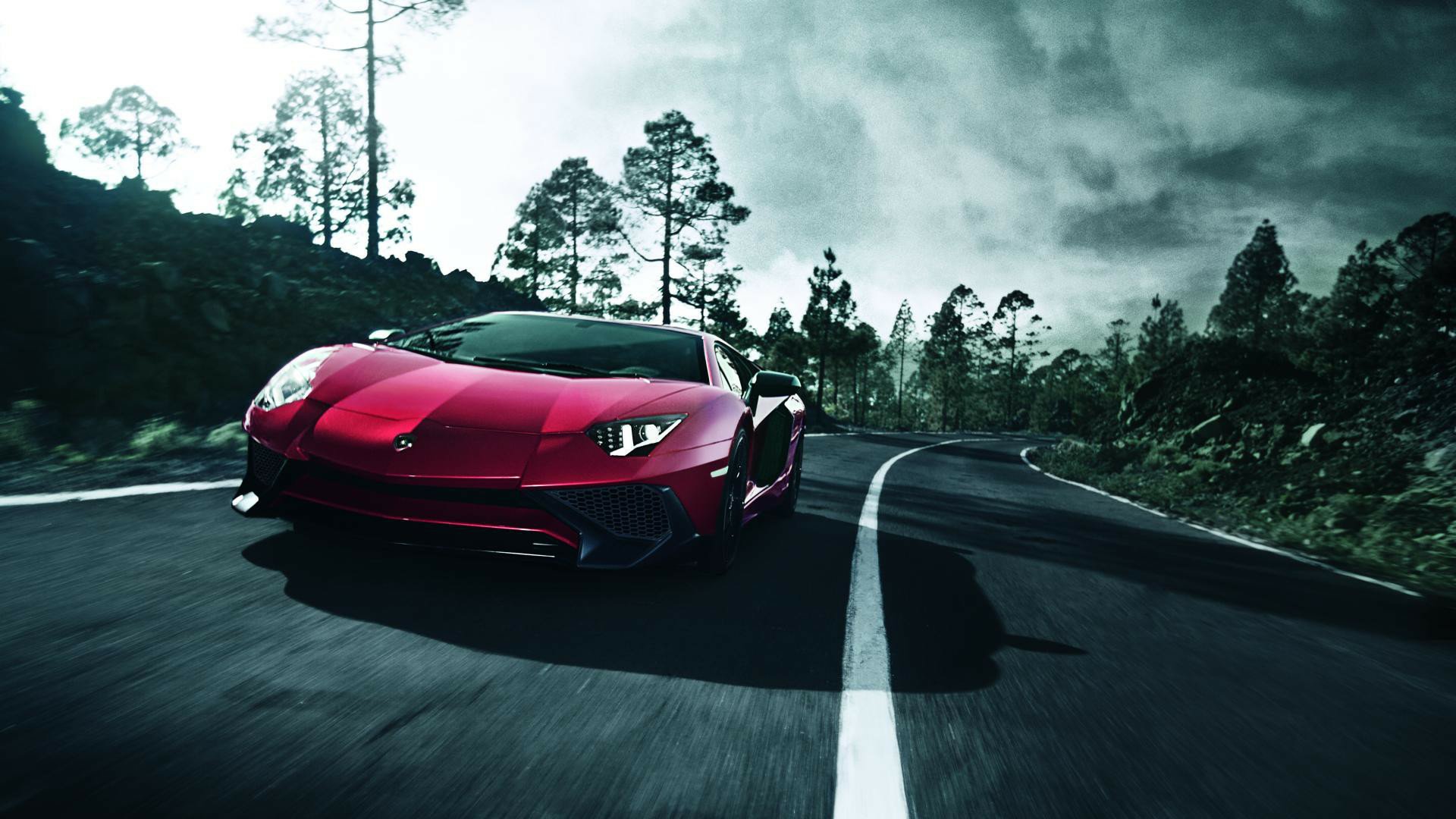 A red Lamborghini Aventador SV supercar driving on a winding road surrounded by trees, captured in high definition as a striking PC desktop wallpaper.