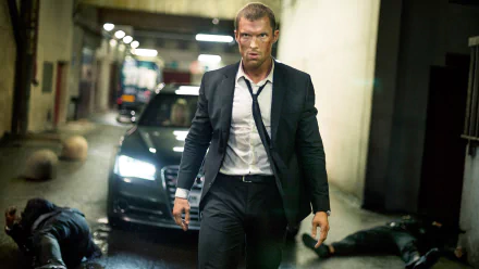 HD PC desktop wallpaper/background: action still from the movie The Transporter Refueled showing a suited man walking away from a black car in an underground garage, tense cinematic lighting.