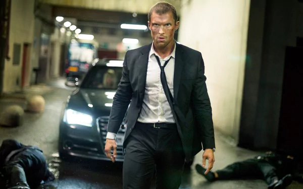 HD PC desktop wallpaper/background: action still from the movie The Transporter Refueled showing a suited man walking away from a black car in an underground garage, tense cinematic lighting.
