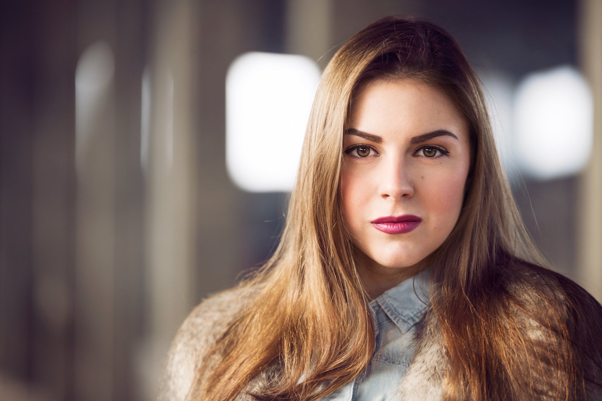 HD desktop wallpaper featuring a brunette woman with brown eyes and lipstick, set against a softly blurred bokeh background.