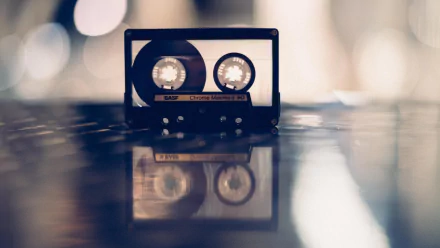 HD PC wallpaper featuring a retro cassette tape in soft focus, evoking nostalgic music vibes with a blurred background and reflective surface.