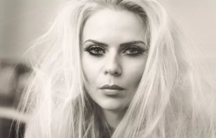 Black and white close-up portrait of a blonde woman with intense eyes, styled as an HD PC desktop wallpaper background.