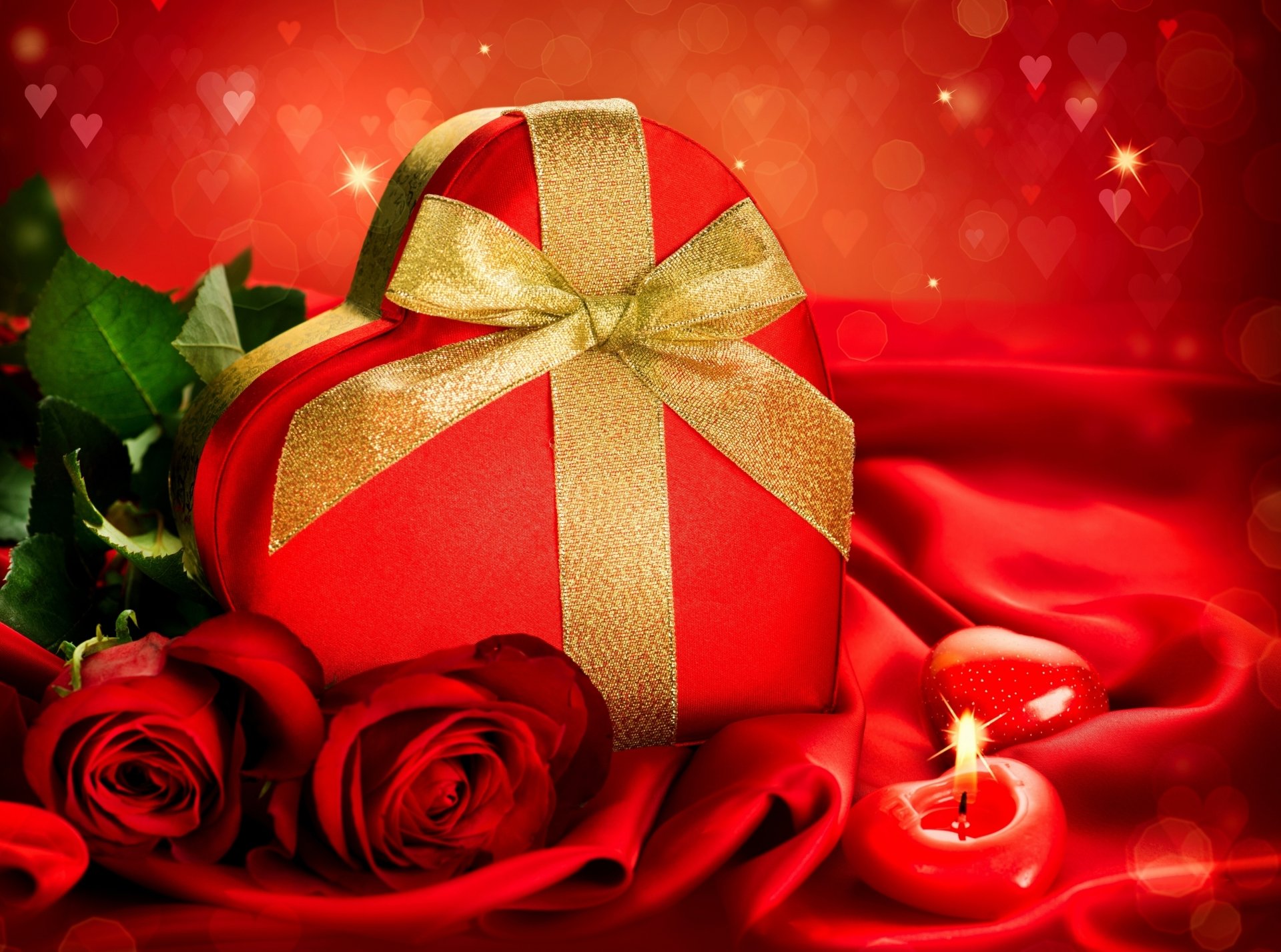 HD desktop wallpaper featuring a heart-shaped red box with a gold ribbon, red roses, a glowing candle, and a romantic Valentine's Day theme.