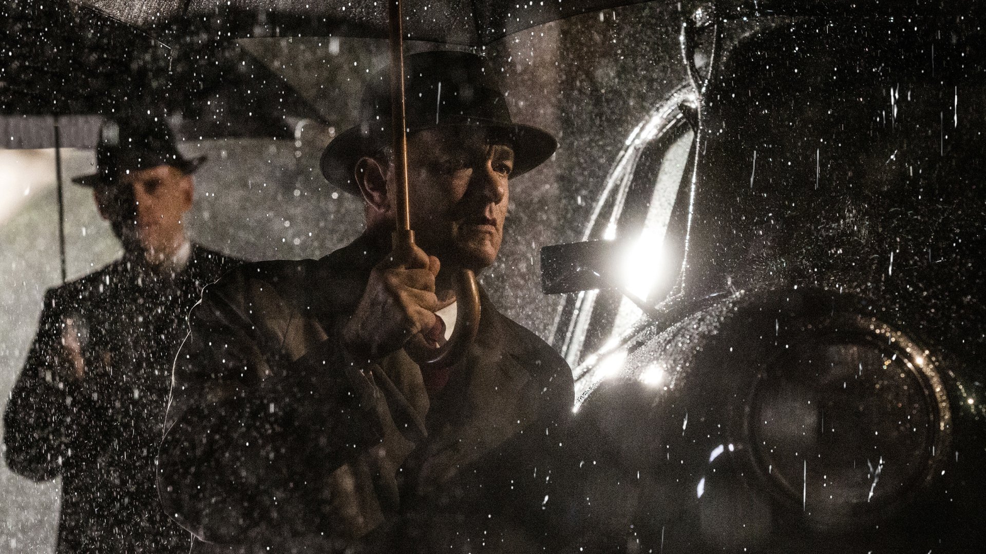 HD PC desktop wallpaper background from the movie Bridge of Spies: two men in vintage coats and hats stand in a rain‑spattered night beside a car, one holding an umbrella.