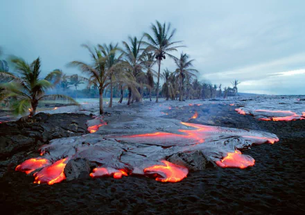 HD PC desktop wallpaper of a volcanic landscape with flowing lava, palm trees, and a smoky sky showcasing dynamic natural volcanic activity.