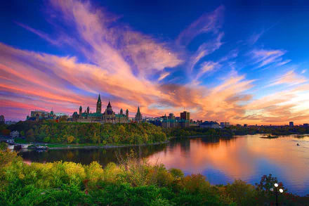 Sunset over Parliament Hill in Canada, with the Parliament buildings reflected in the lake, set against a vibrant sky in this HD cityscape wallpaper.