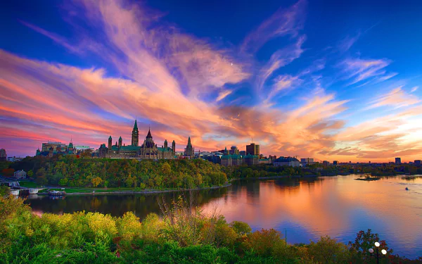 Sunset over Parliament Hill in Canada, with the Parliament buildings reflected in the lake, set against a vibrant sky in this HD cityscape wallpaper.