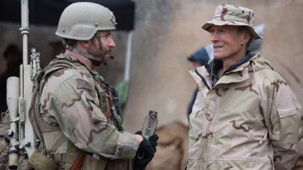A scene from the movie American Sniper, featuring Clint Eastwood interacting with a soldier in military attire. This HD wallpaper captures a moment of camaraderie amid a military backdrop.