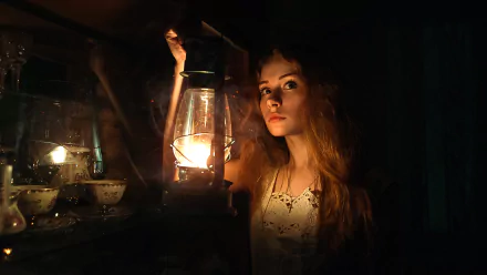 A woman with red hair and brown eyes holds a lantern, casting a warm glow. The dimly lit setting gives a mysterious and enchanting vibe, making it a captivating HD desktop wallpaper background.