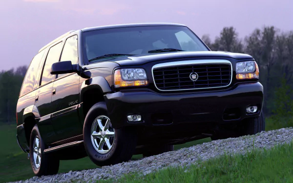 HD desktop wallpaper featuring a black Cadillac Escalade parked on a gravel path with a natural landscape and purple sky background.