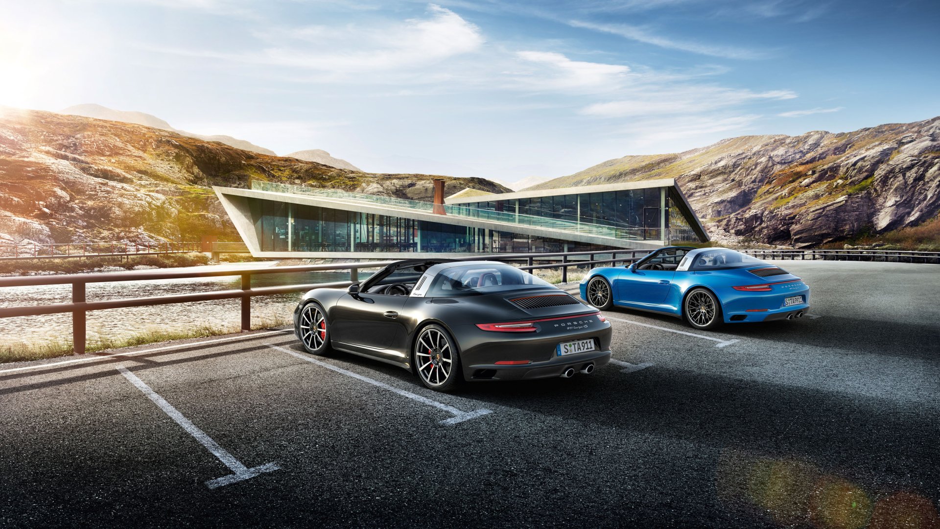 2K Quad HD PC wallpaper showing two Porsche 911 Targa vehicles: a black Porsche 911 car and a blue Porsche 911 parked by a modern waterside building.