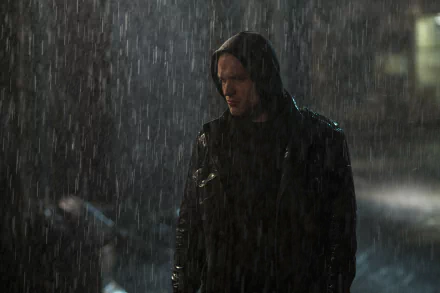 A moody scene featuring Ed Skrein in a hooded jacket, standing in heavy rain, capturing a dramatic moment from the movie Deadpool in a 4K Ultra HD background.