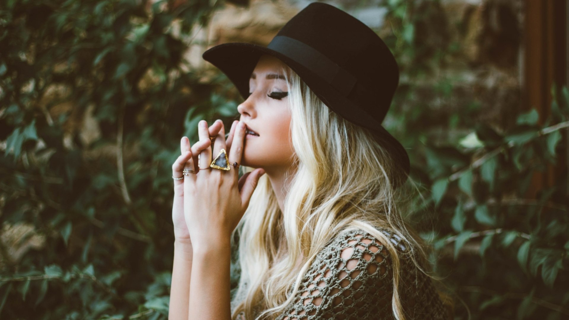 Blonde woman wearing a black hat and rings, eyes closed in a pensive pose against soft bokeh — 4K Ultra HD PC desktop wallpaper mood portrait.