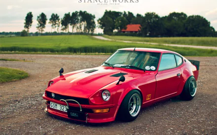A striking red JDM vehicle parked on a gravel road, surrounded by lush greenery, showcasing its sleek design and customized details. An HD wallpaper capturing automotive passion.