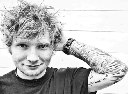 Black and white HD desktop wallpaper featuring Ed Sheeran with tattoos, smiling with a hand behind his head, capturing the essence of the English singer.