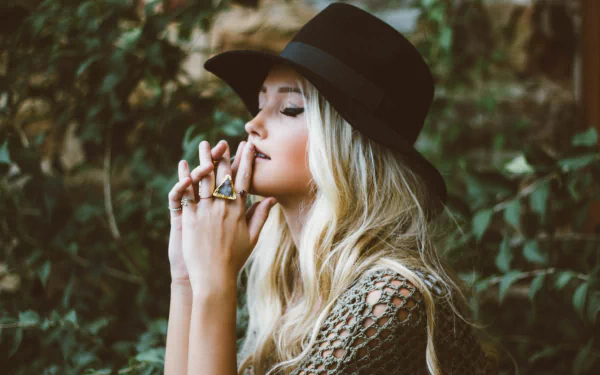Blonde woman wearing a black hat and rings, eyes closed in a pensive pose against soft bokeh — 4K Ultra HD PC desktop wallpaper mood portrait.