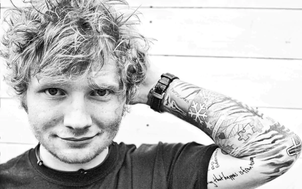 Black and white HD desktop wallpaper featuring Ed Sheeran with tattoos, smiling with a hand behind his head, capturing the essence of the English singer.