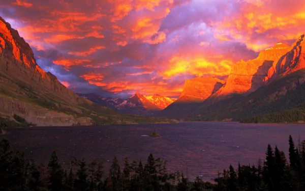 Stunning sunset over a tranquil lake in Glacier National Park, Alberta, Canada, with vibrant purple and orange hues illuminating the mountain landscape and dramatic cloud formations.