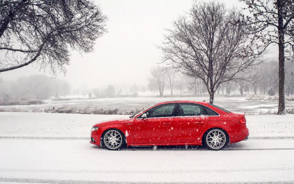 A red Audi S4 car parked on a snowy winter road with snowfall, surrounded by bare trees in a serene, snow-covered landscape.