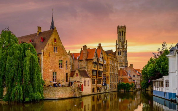 Sunset over the canal in Bruges, Belgium, featuring historic buildings and a prominent church tower, captured as an HD desktop wallpaper and background.
