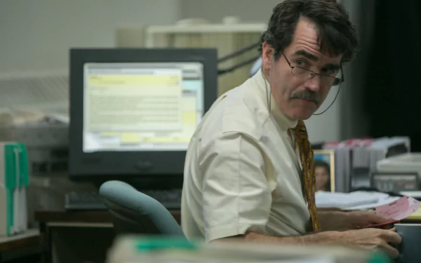 Scene from Spotlight (2015): bespectacled man in shirt and tie at a cluttered newsroom desk, turning toward the camera. 2K Quad HD PC desktop wallpaper/background.