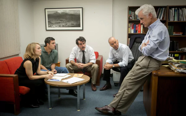 Cast members including Mark Ruffalo and Rachel McAdams, portraying journalists in the Spotlight (2015) movie, in a focused newsroom discussion scene.