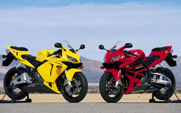HD PC desktop wallpaper featuring two Honda CBR600RR motorcycles, one yellow and one red, parked side by side against a clear sky background.