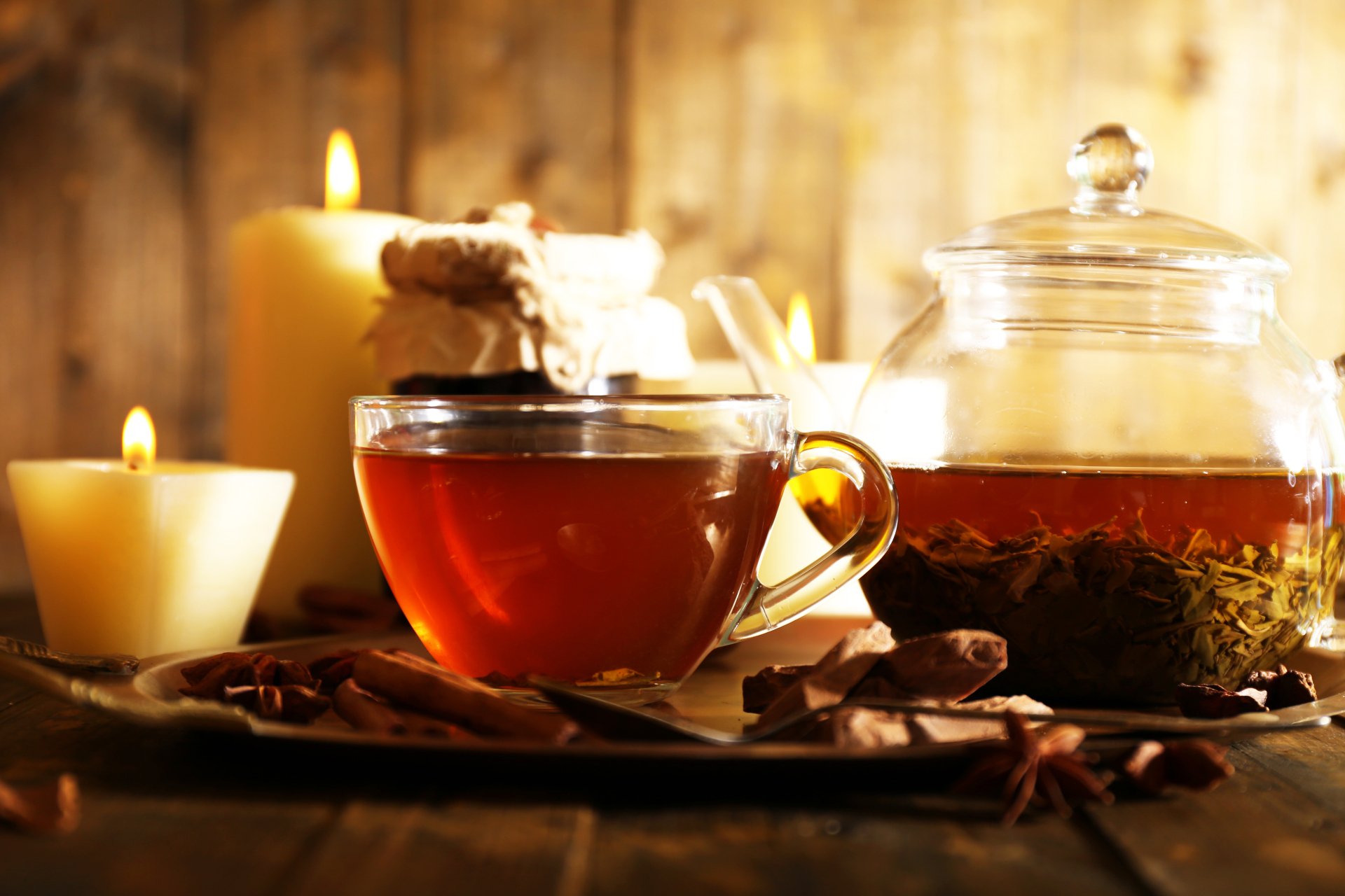 A cozy 4K Ultra HD desktop wallpaper showing a cup of tea with anise and cinnamon sticks, surrounded by lit candles and a glass jar of tea leaves.