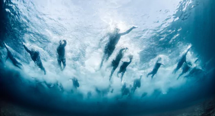 HD PC desktop wallpaper of swimmers underwater — silhouetted athletes racing above, bubbles and sunlight streaming from below, sports action.