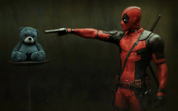 Deadpool, in his signature red and black suit, points a gun at a blue teddy bear placed on a small table, creating a humorous and unusual desktop wallpaper in HD quality.