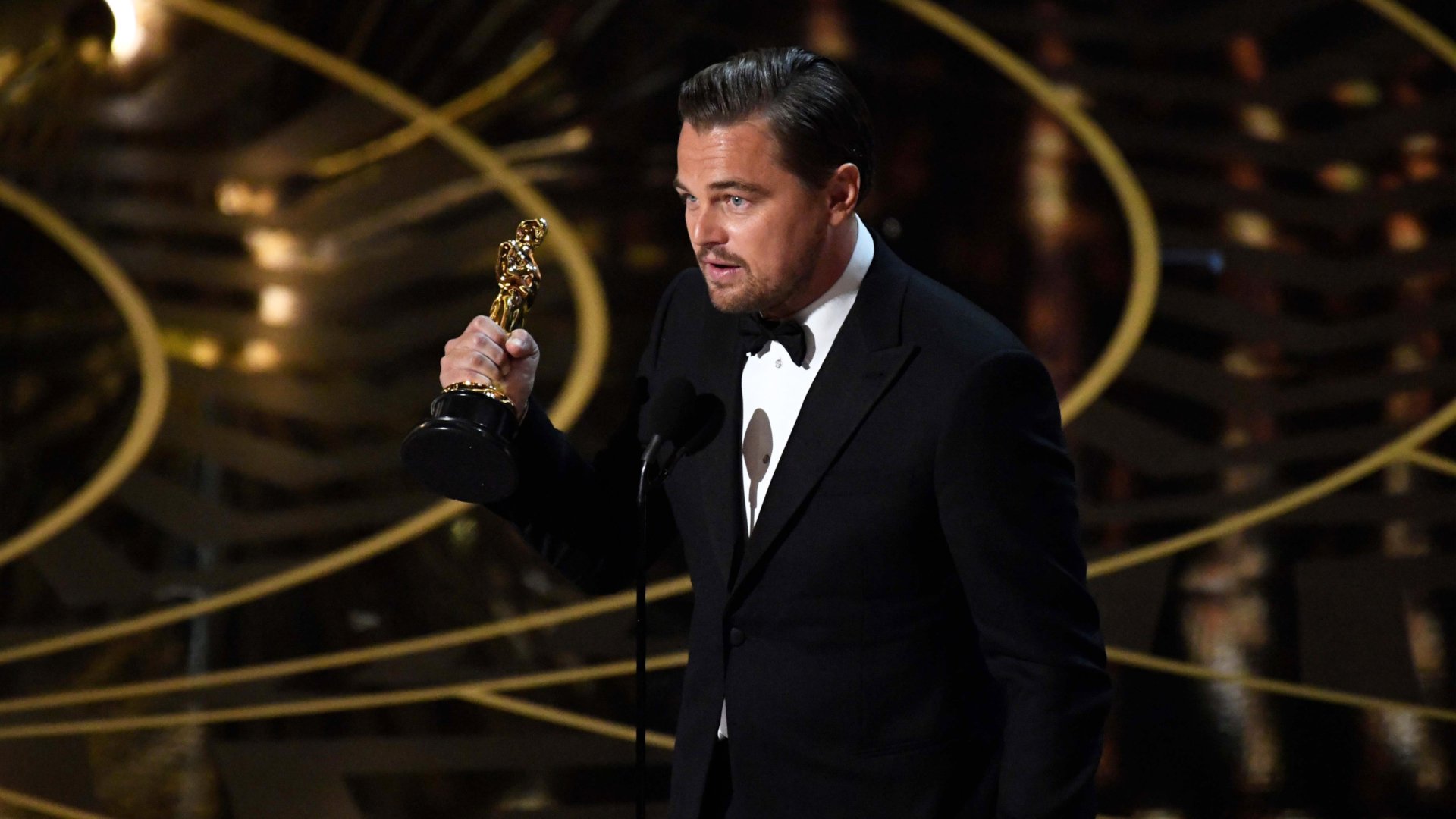 HD desktop wallpaper featuring celebrity Leonardo DiCaprio holding an Oscar statuette during an awards ceremony.