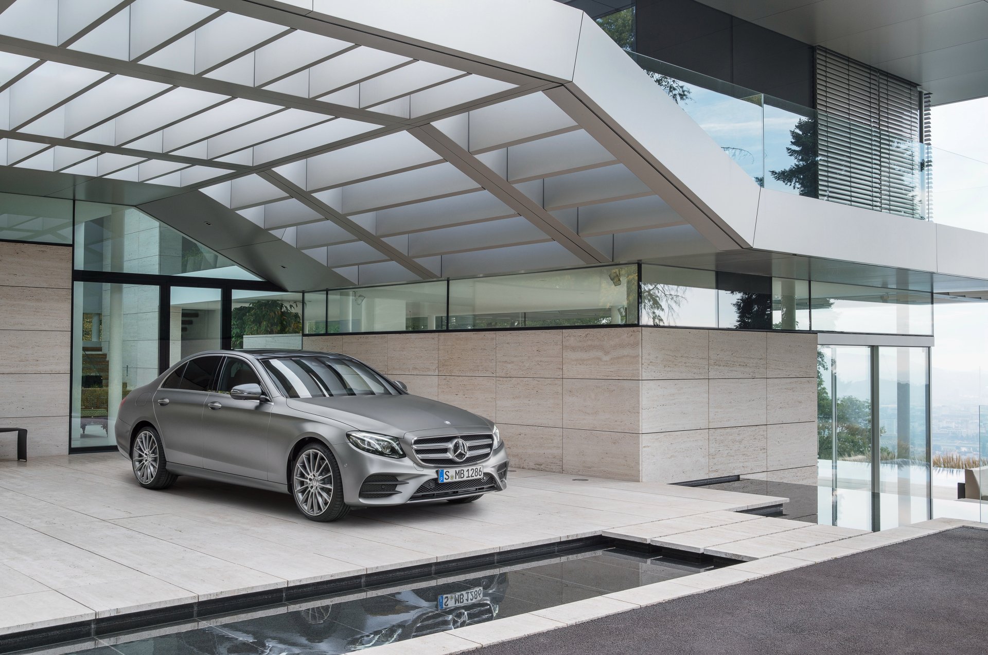Silver Mercedes-Benz E-Class sedan parked by a modern glass and stone building, captured in a high-resolution 4K Ultra HD wallpaper.