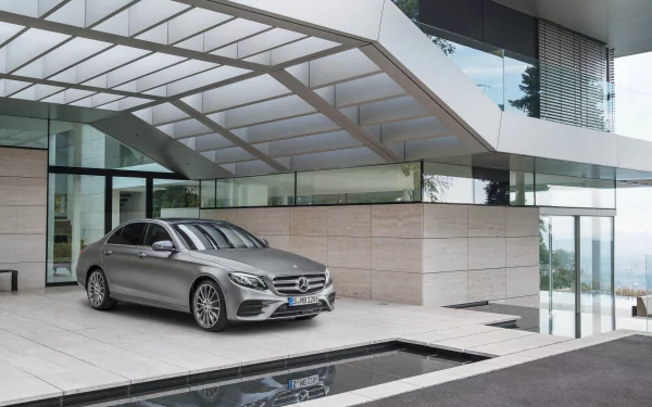 Silver Mercedes-Benz E-Class sedan parked by a modern glass and stone building, captured in a high-resolution 4K Ultra HD wallpaper.