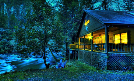 A serene HD desktop wallpaper featuring a cozy house with a lit porch at dusk, nestled beside a tranquil river and surrounded by trees. The scene is enhanced with vibrant HDR effect.