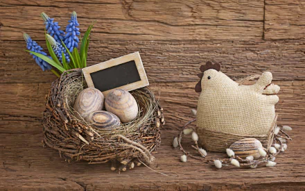 A charming HD desktop wallpaper of an Easter nest with eggs, a small chalkboard, blue flowers, and a fabric chicken on a rustic wooden background.